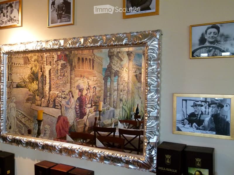 Elegant room with a large ornate mirror reflecting a detailed mural, several framed pictures on the walls, a small table with chairs, and decorative candles.