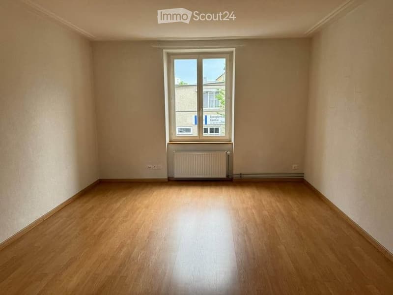 Empty room with wooden flooring, white walls, a single window, and a radiator below it.