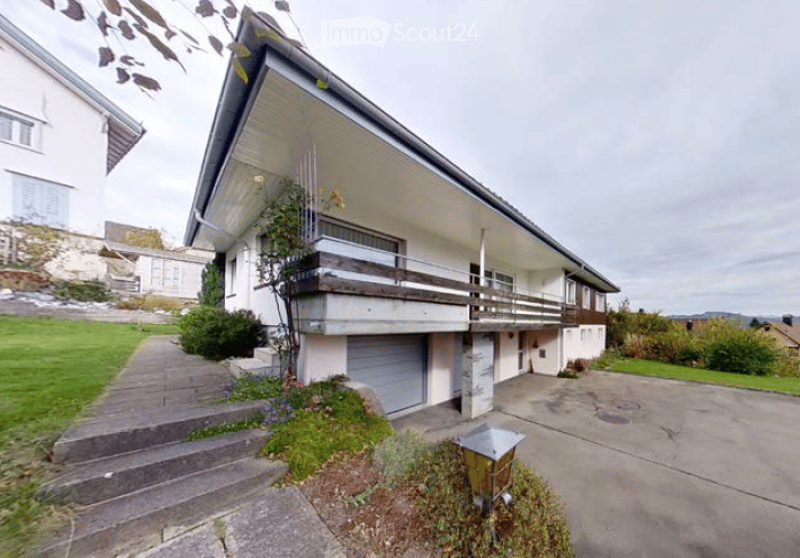 Two-story house with a balcony, garage, and a well-maintained lawn.