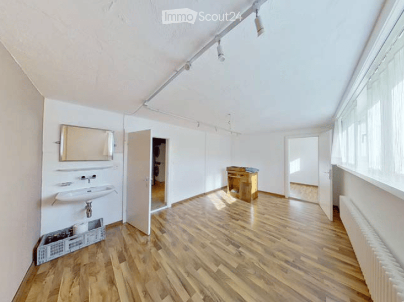 Empty room with wooden flooring, white walls, and a sink in the corner. There is a small cabinet and a mirror on the wall.