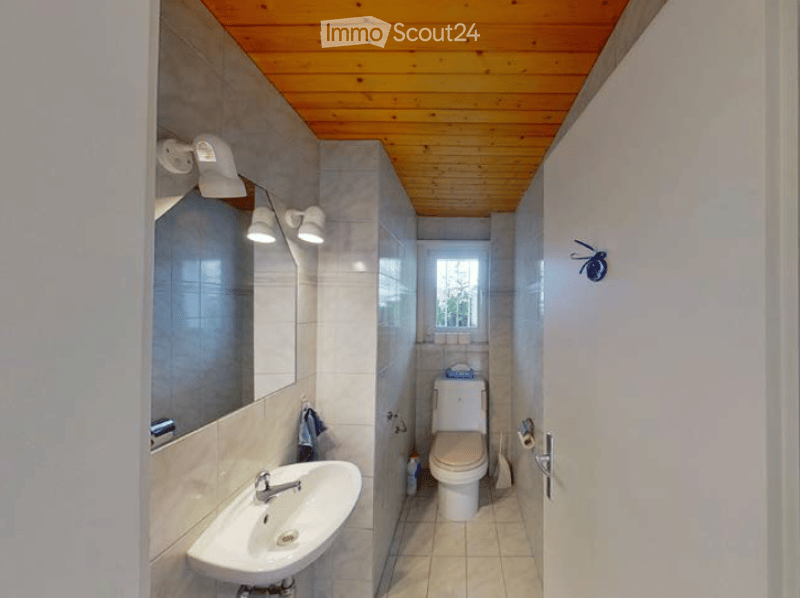 Bathroom with a wooden ceiling, tiled walls, a sink with a faucet, a toilet, a mirror, and light fixtures.