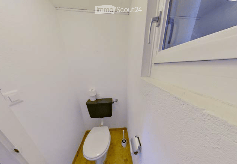 Small bathroom with white walls, a toilet, and a window. Toilet paper is placed on the toilet tank and on a holder next to the toilet.