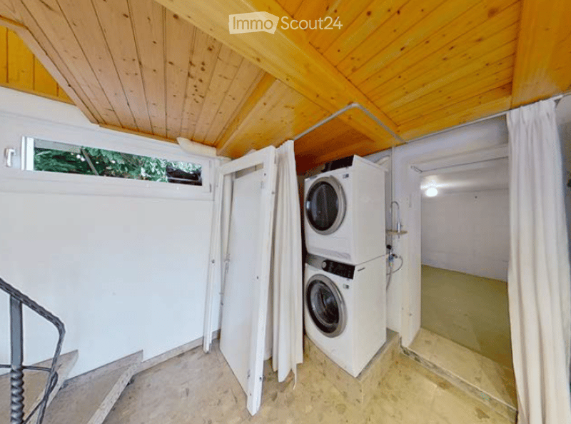 Laundry room with a private washing machine and dryer, wooden ceiling, and a window with a view of greenery.