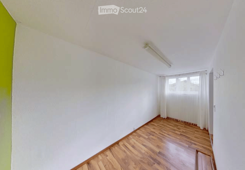 Empty room with white walls, wooden flooring, and a window with white curtains. No furniture or equipment is present.