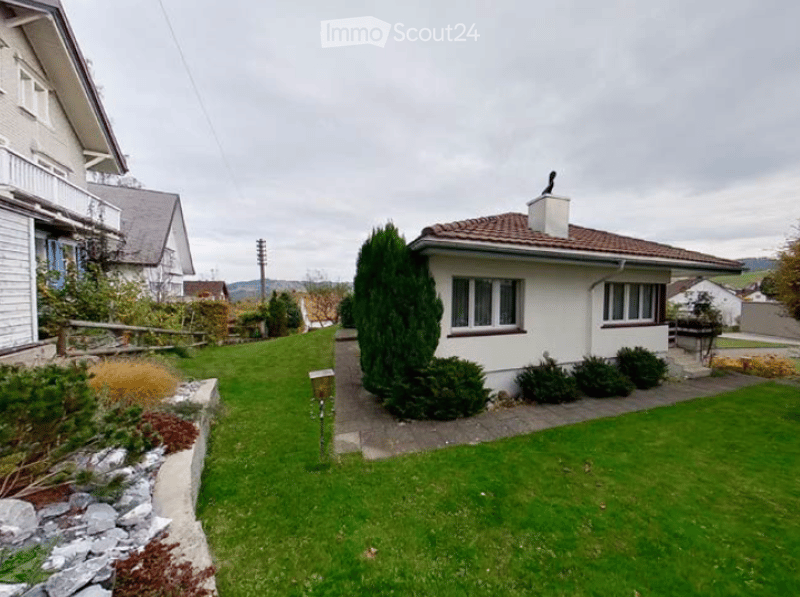 Single-family house with a well-maintained garden, featuring a white exterior, red-tiled roof, and neatly trimmed hedges.