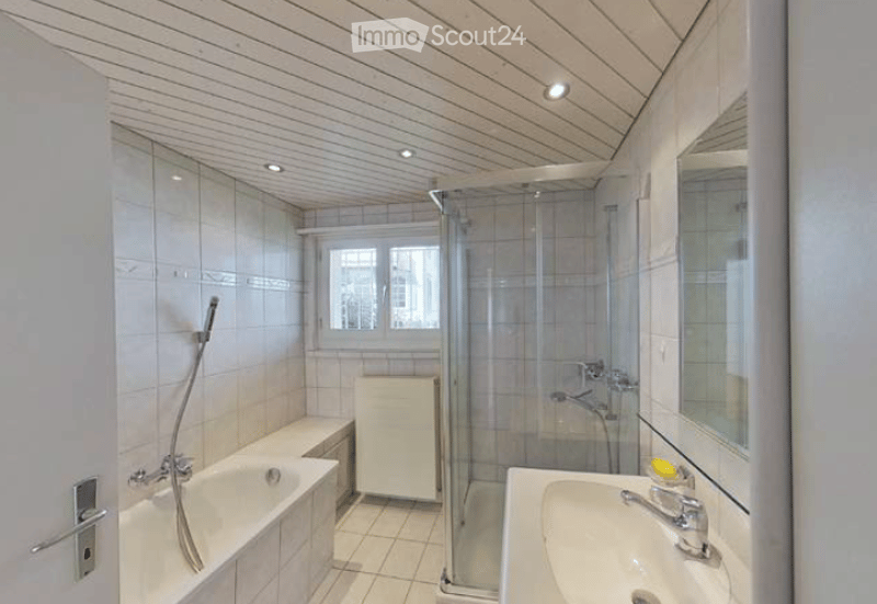 Modern bathroom with a bathtub, sink, mirror, glass-enclosed shower, and a small cabinet. The room features white tiles and a view of the city through a window.