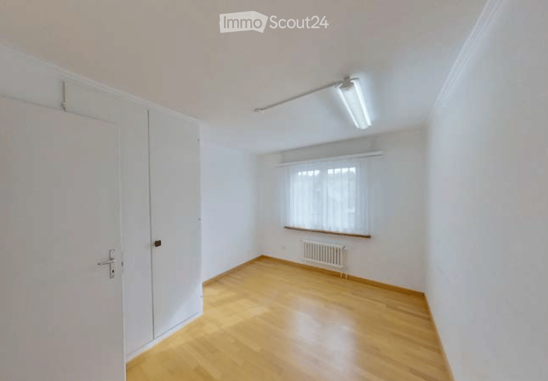 Empty room with wooden flooring, white walls, a window with white blinds, a radiator, and a built-in closet with white doors.