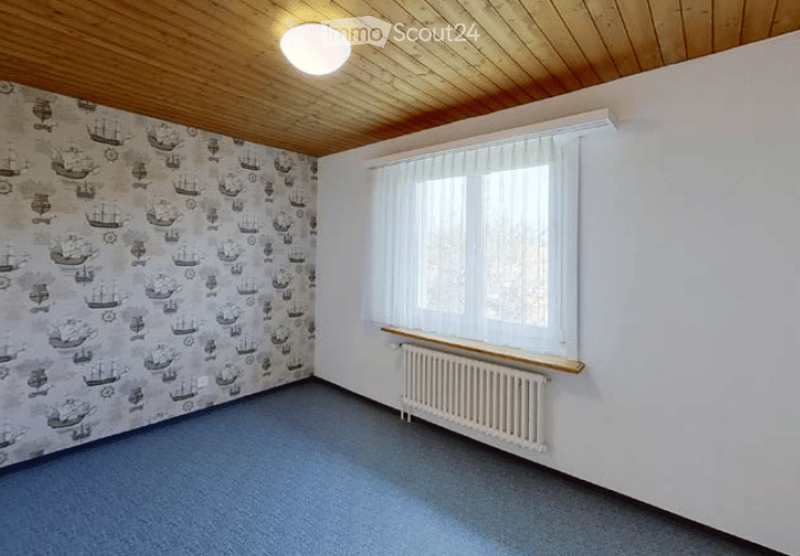Empty room with wooden ceiling, blue carpet, white radiator, and large window with white curtains.