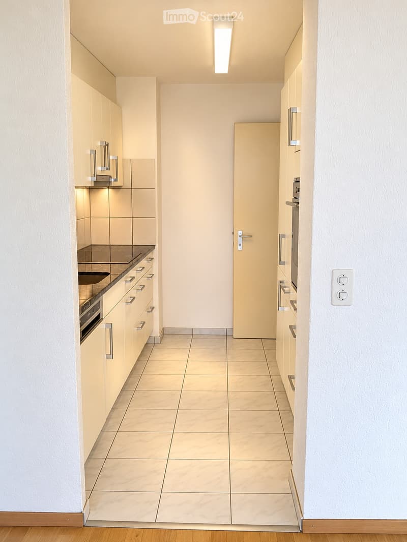 Modern kitchen with light-colored cabinets, a sink, and an oven, featuring tiled flooring and recessed lighting.