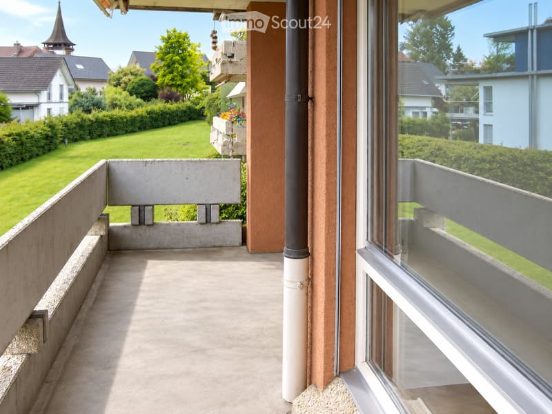 Balcony with concrete floor, glass railing, and view of a green lawn and neighboring houses.