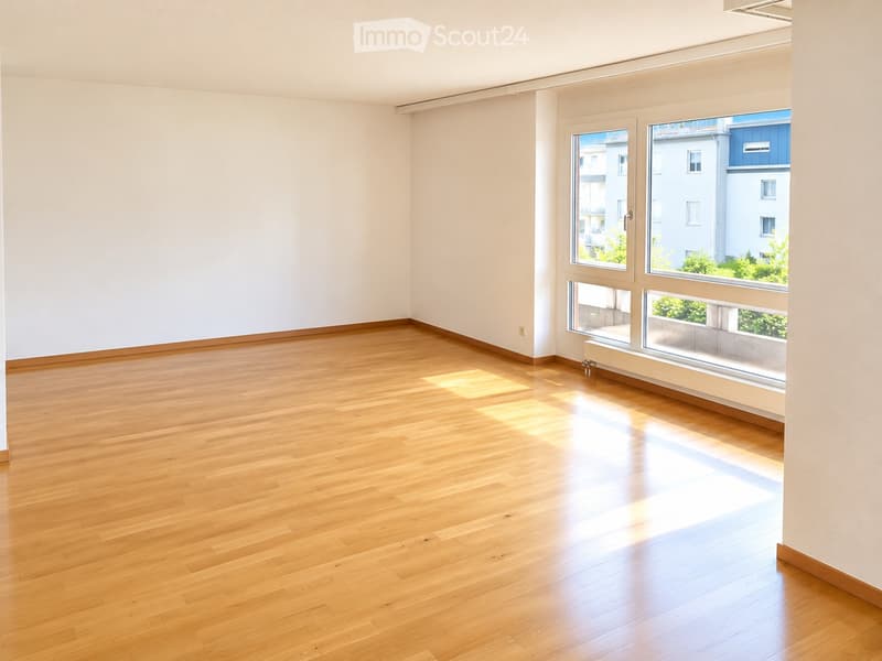 Empty room with wooden flooring and large windows, allowing natural light to fill the space.