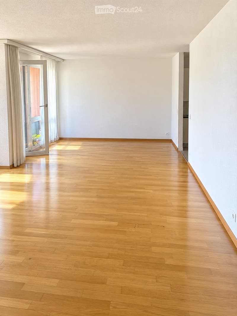 Empty room with wooden flooring, white walls, and a sliding glass door with curtains leading to a balcony.