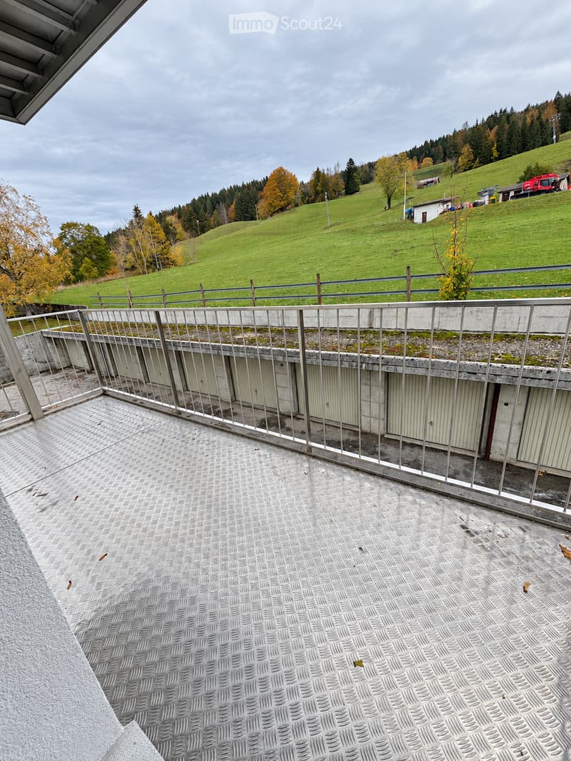 Balcony with metal railing, tiled floor, and view of green hills and scattered houses.