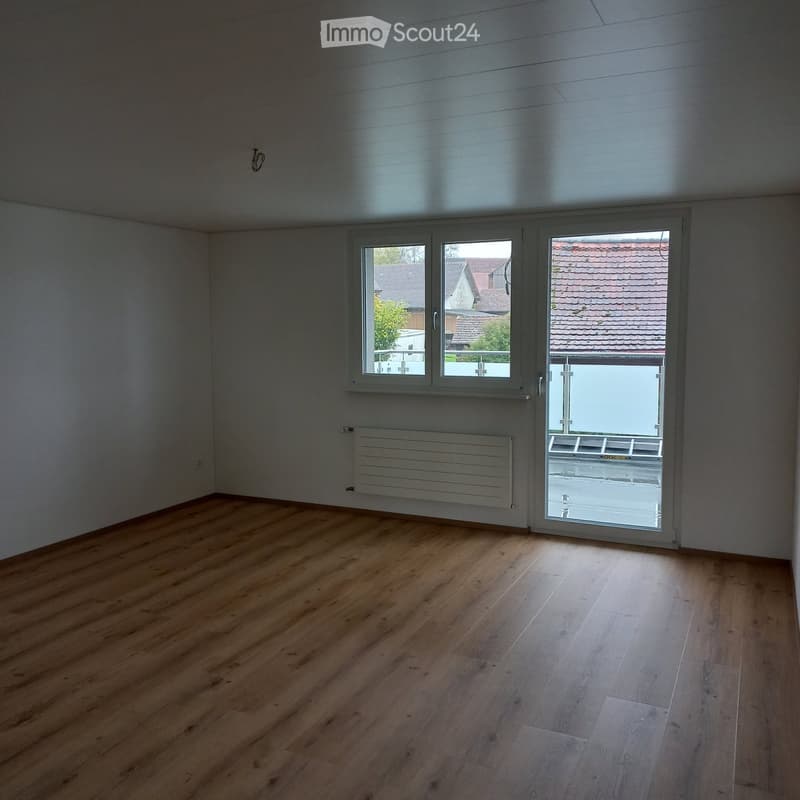 Empty room with wooden flooring, white walls, large windows, and a radiator. No furniture or equipment present.