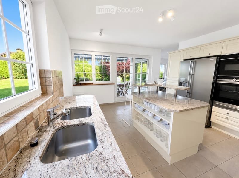 Modern kitchen with granite countertops, double sink, stainless steel appliances, and ample cabinet space. Large windows provide natural light and a view of the garden.