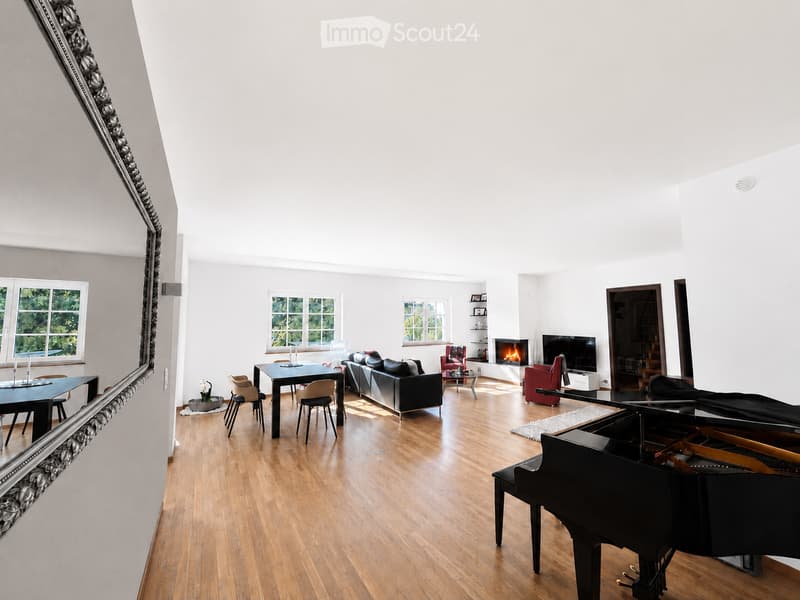 Bright, open living space with wooden flooring, large windows, a black grand piano, a fireplace, a television, and seating areas including a sofa and chairs.