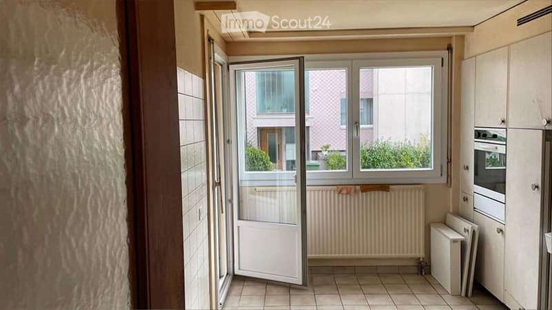 Empty room with tiled floor, white walls, and an open sliding door leading to a balcony. The room has built-in cabinets and a radiator.