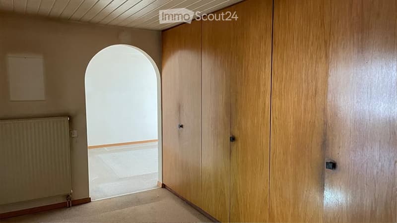 Empty room with wooden built-in wardrobes, a radiator, and an arched doorway leading to another space.