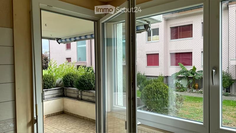 Balcony with tiled floor, open sliding doors, view of neighboring building and greenery.