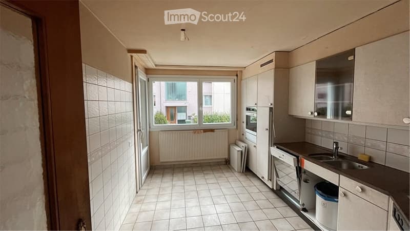 Modern kitchen with white tiled walls and floor, white cabinets, a sink with a faucet, an oven, and a refrigerator. A window with a view of the outside is present.