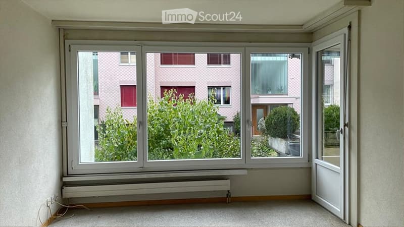 Empty room with large windows, radiator, and a door leading outside. No furniture or equipment present.