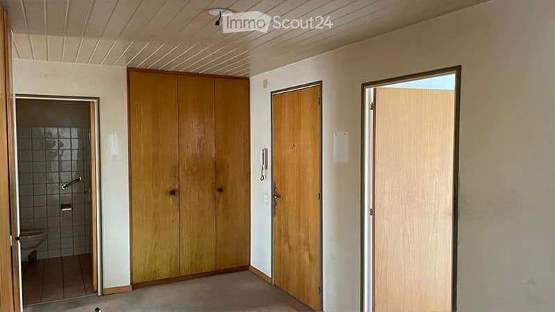 Empty room with wooden closet, wooden doors, and a visible bathroom area with tiled walls and a bathtub.