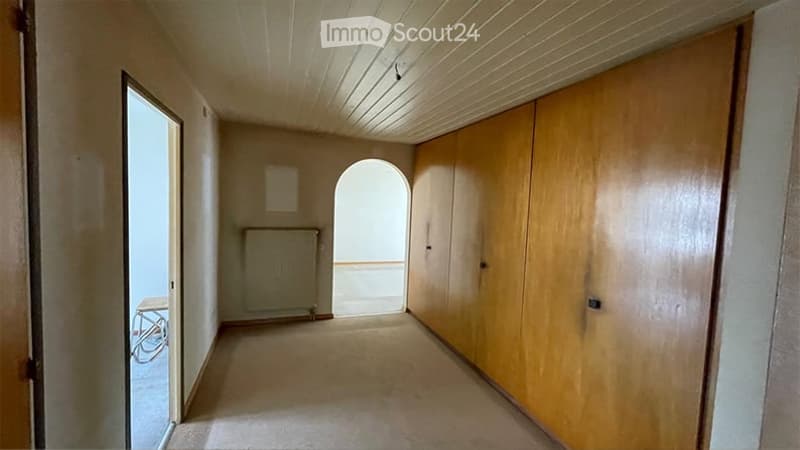 Empty hallway with wooden paneling, a radiator, and an arched doorway leading to another room.