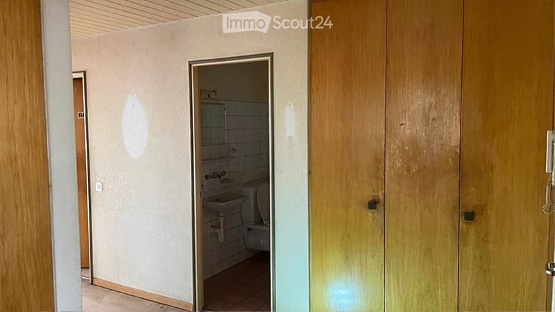 Small bathroom with a sink and toilet, visible through an open door. The walls are tiled, and the floor is covered with tiles.