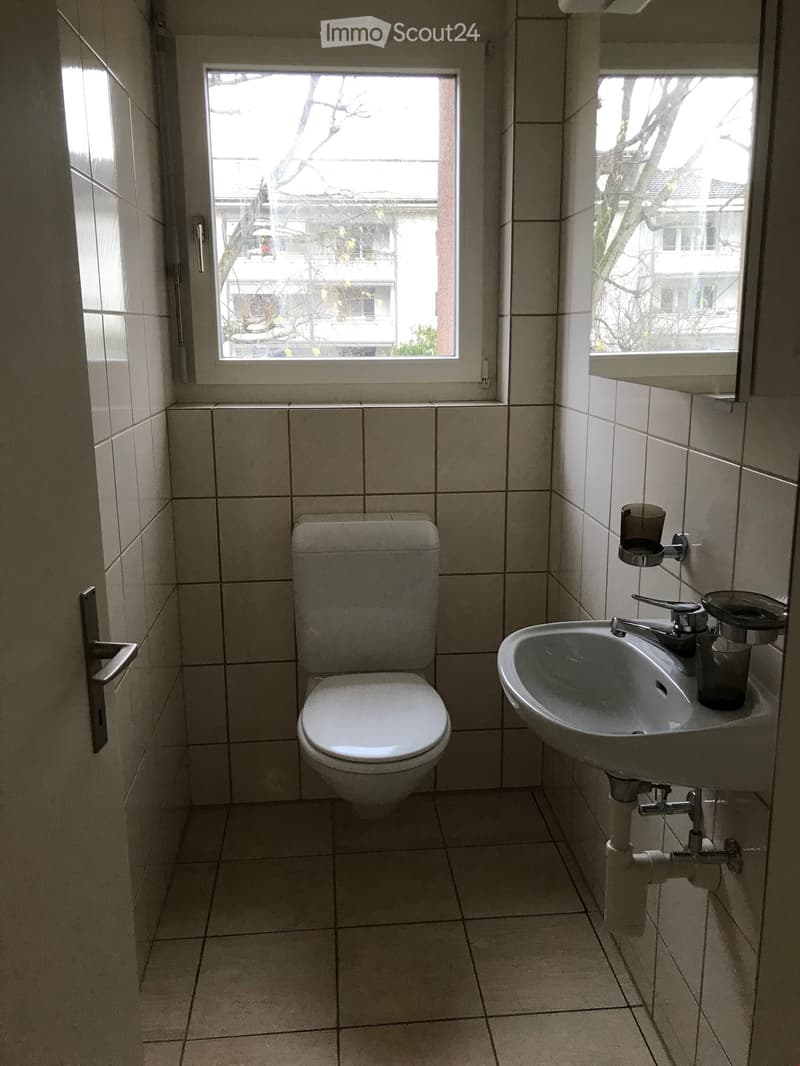 Small bathroom with tiled walls and floor, featuring a toilet, sink with faucet, and a cup on the sink.