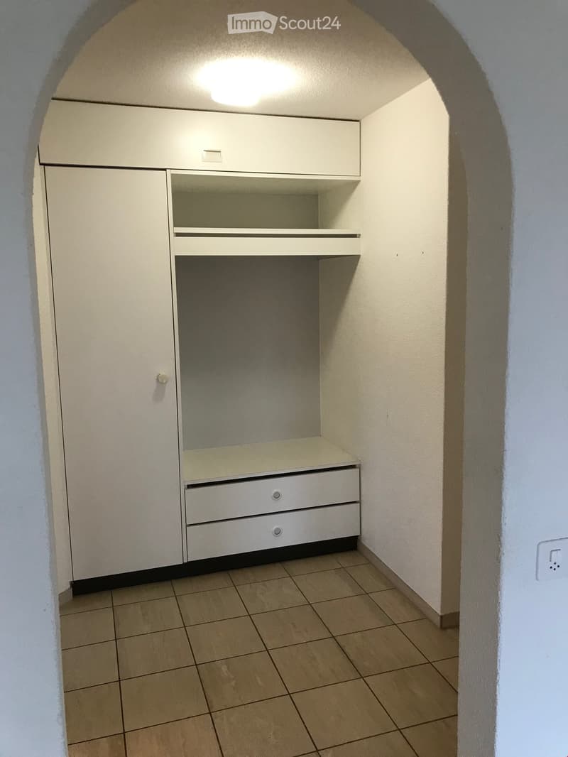Empty room with tiled floor, white walls, built-in cabinet with drawers and shelves, and a small window at the top.