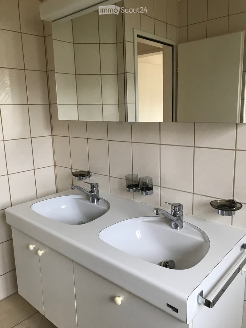Modern bathroom with a double sink vanity, chrome faucets, a large mirror, and two small cups on the counter.