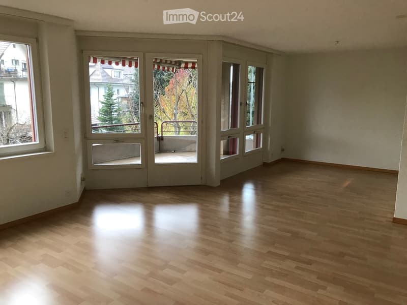 Empty room with wooden flooring, large windows, and sliding glass doors leading to a balcony.