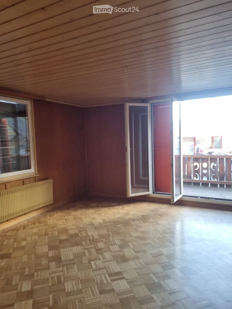 Empty room with wooden parquet flooring, glass windows, door, and balcony.