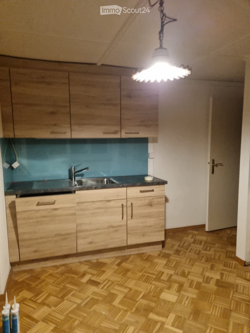 wooden cabinets, blue backsplash, stainless steel sink, granite countertop, wooden floor, modern lighting fixture, open door