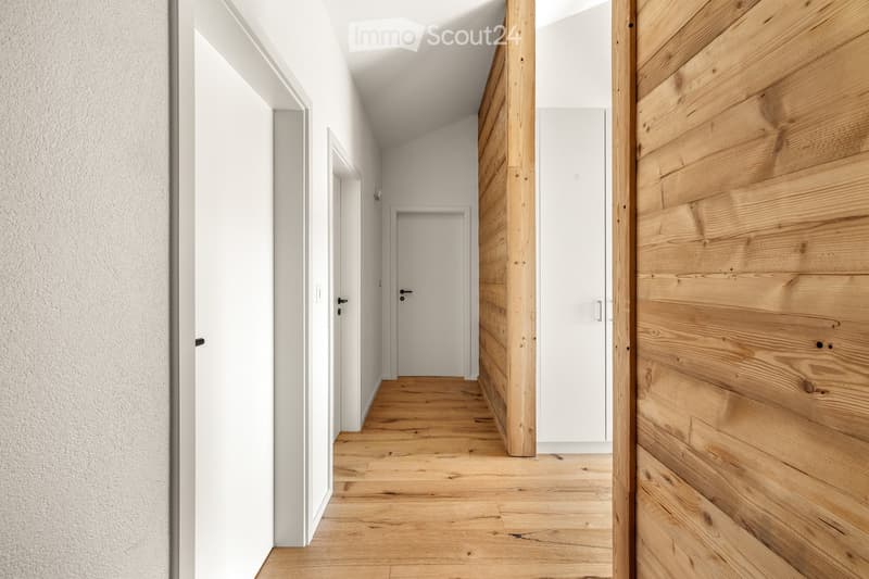 Modern hallway with wooden flooring, white walls, and several closed doors.