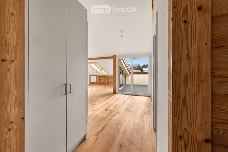 Bright hallway with wooden flooring, white walls, and a sliding glass door leading to a balcony area with wooden decking and a skylight above.