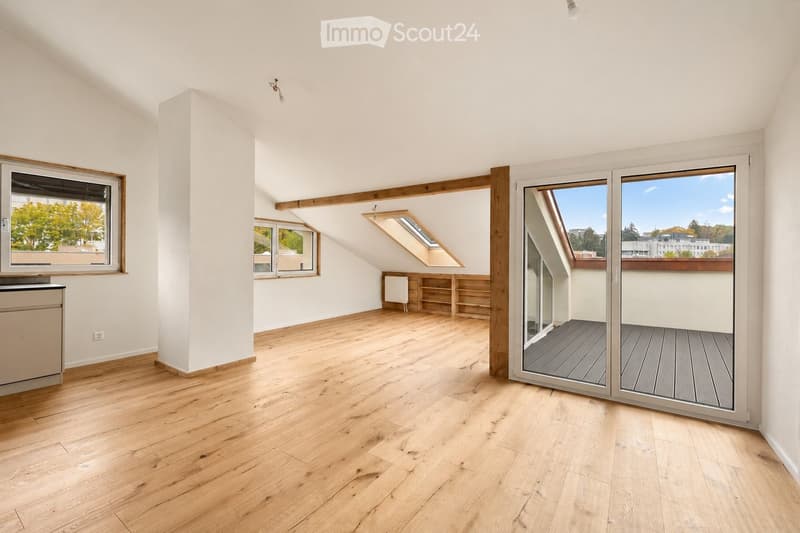 Bright, empty attic room with wooden flooring, white walls, large windows, and a sliding glass door leading to a balcony.