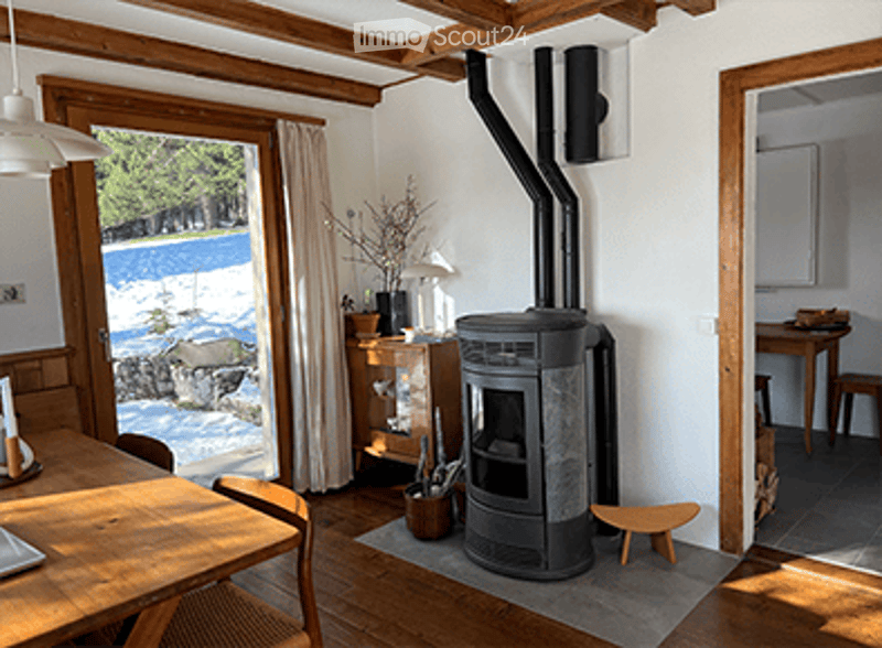 A cozy, rustic living room with wooden beams, a wood-burning stove, a dining table, and wooden furniture.