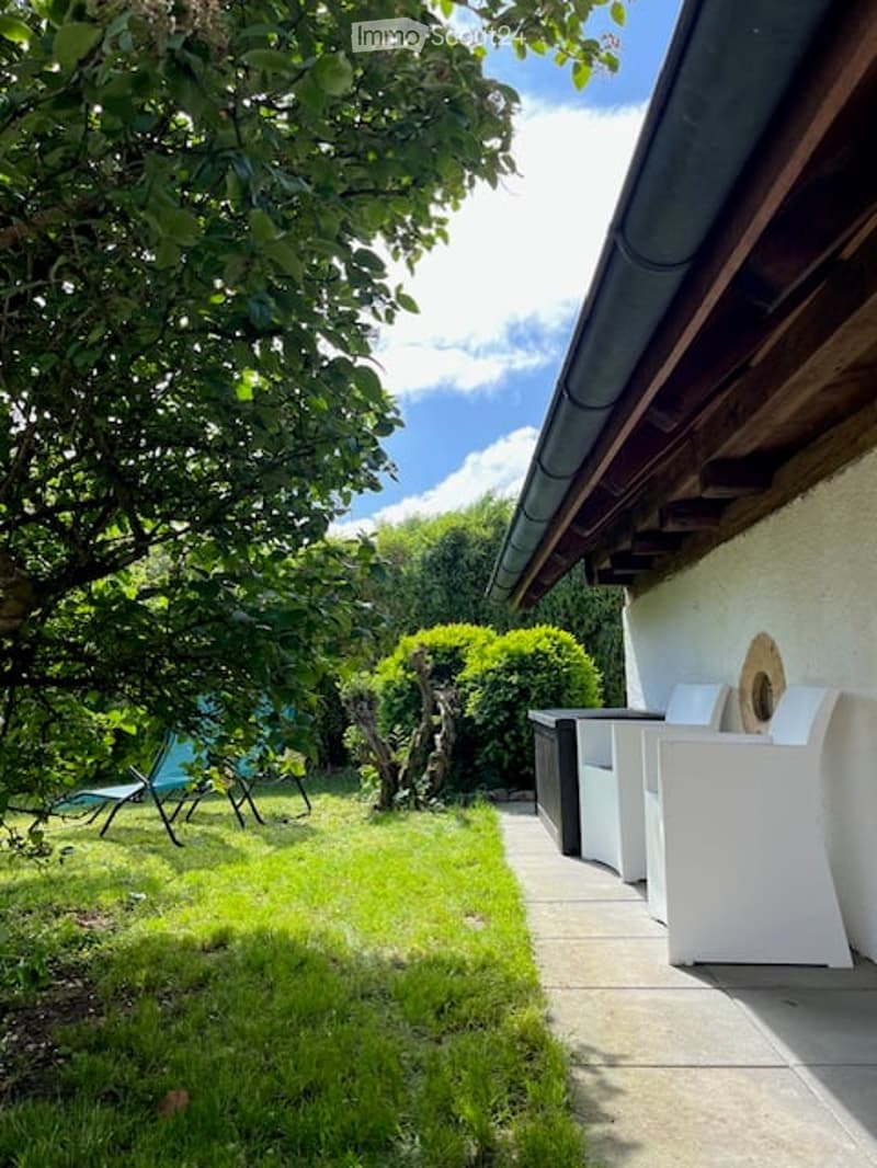 Green lawn, shrubs, lounge chairs, patio with lounge chairs, trash bins, white chairs