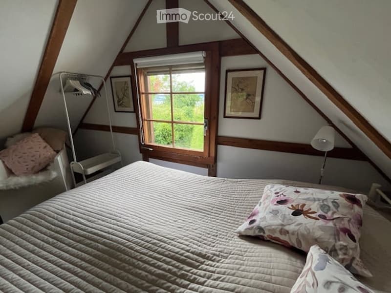 Bedroom with wooden ceiling, bed, pillow, bedsheet, lamp, windows with shutter, chair, framed artwork