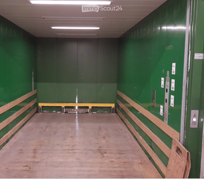 Elevator shaft with green walls, wooden floor, and control panel on the right side.
