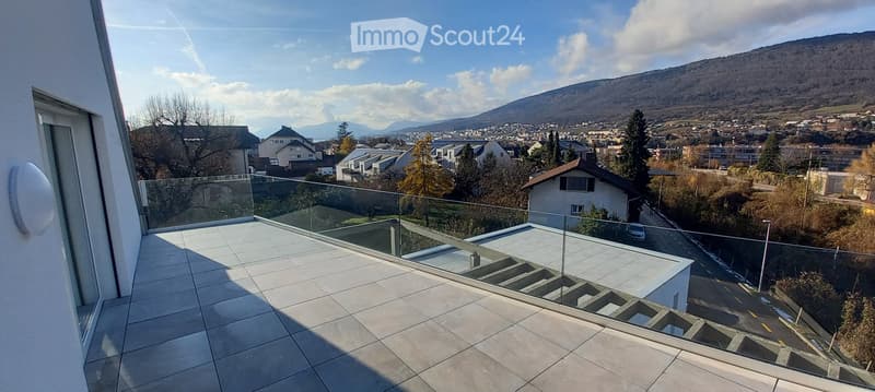 Modern balcony with glass railing, tiled floor, and scenic city and mountain view.