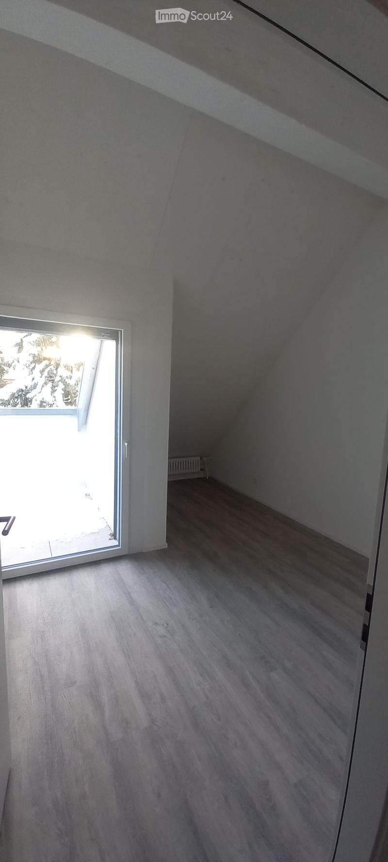 Empty room with wooden flooring, white walls, and a large window with a view of greenery outside.