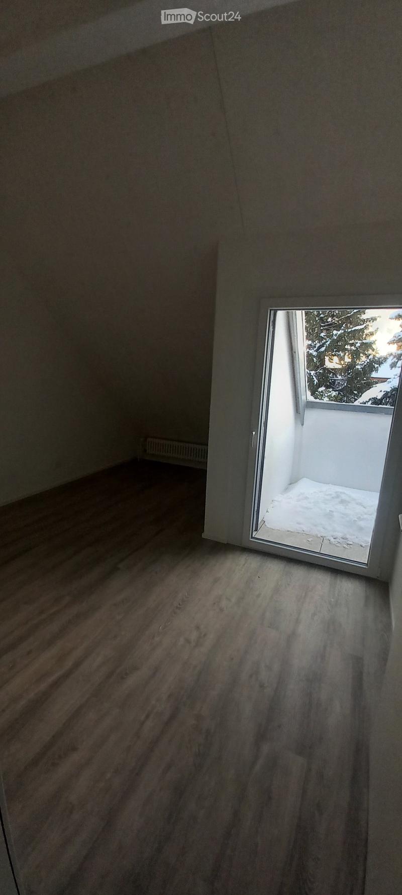 Empty room with wooden flooring and a sliding glass door leading to a snowy outdoor area.