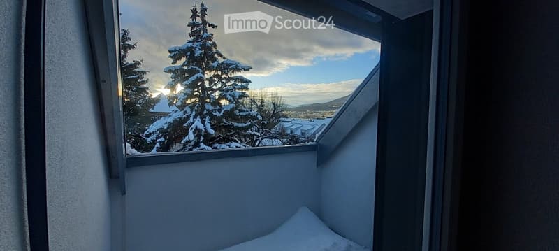 Snow-covered balcony with a view of snow-laden trees and distant houses.
