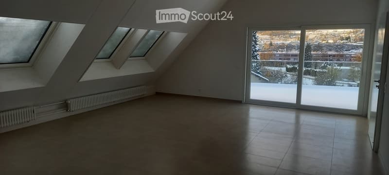 Empty attic room with skylights, large window offering a snowy landscape view, tiled floor, and radiator.