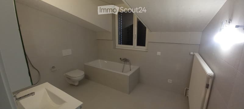 Modern bathroom with a bathtub, toilet, sink, and window. Light-colored tiles and sleek fixtures.