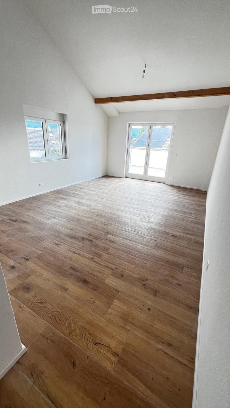 Empty room with wooden flooring, white walls, and large windows, including a sliding glass door leading outside.