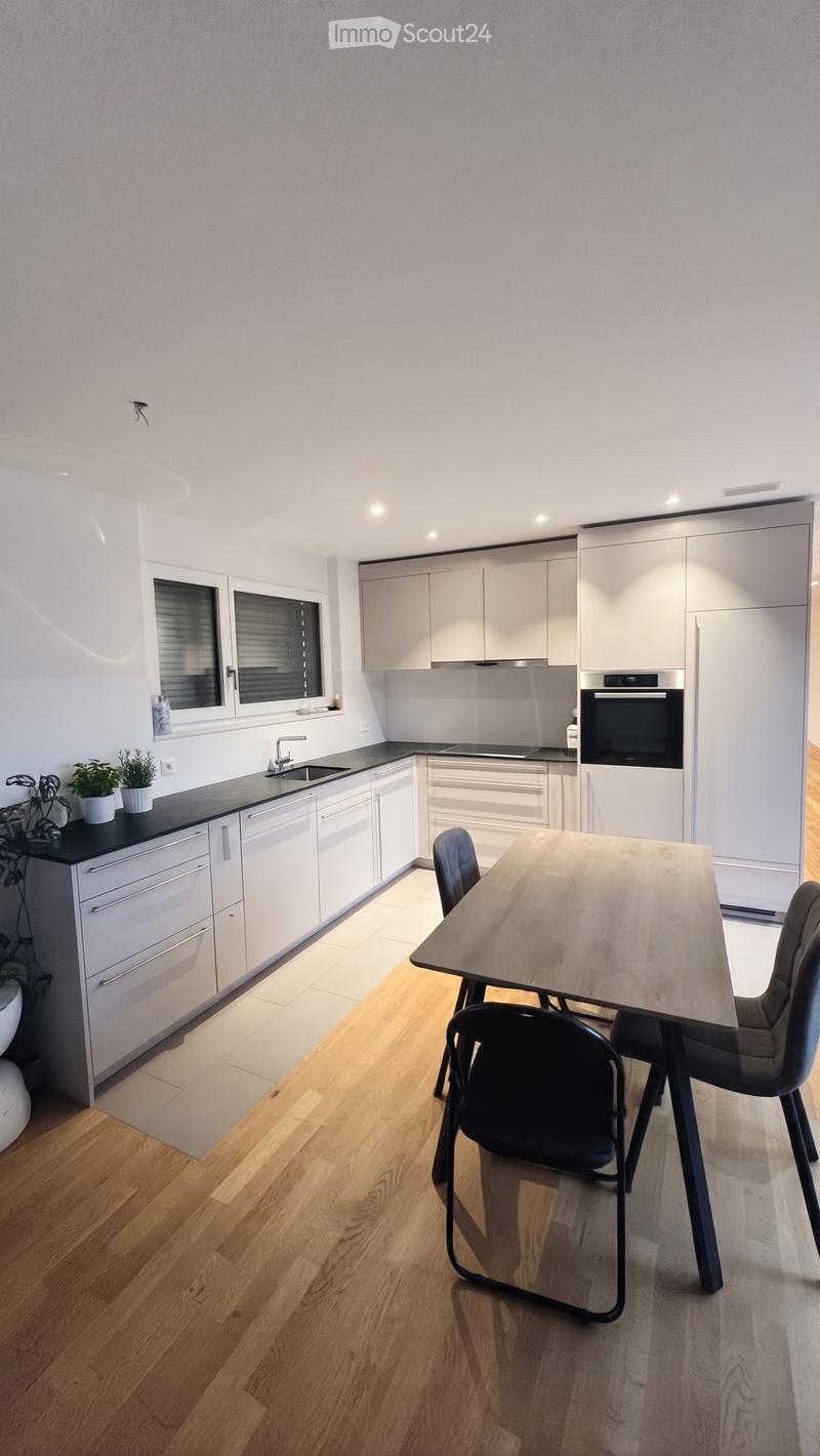 Modern kitchen with white cabinets, a central island, and a dining area featuring a table and chairs. The space includes a sink, oven, and refrigerator, with a potted plant on the counter.