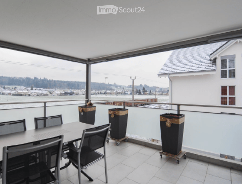 Balcony with a view of a cityscape, featuring a table and chairs, and trash bins.